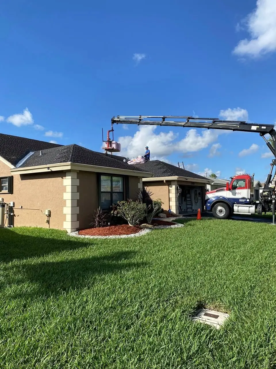 Boom truck delivering roofing materials to a home under a clear blue sky