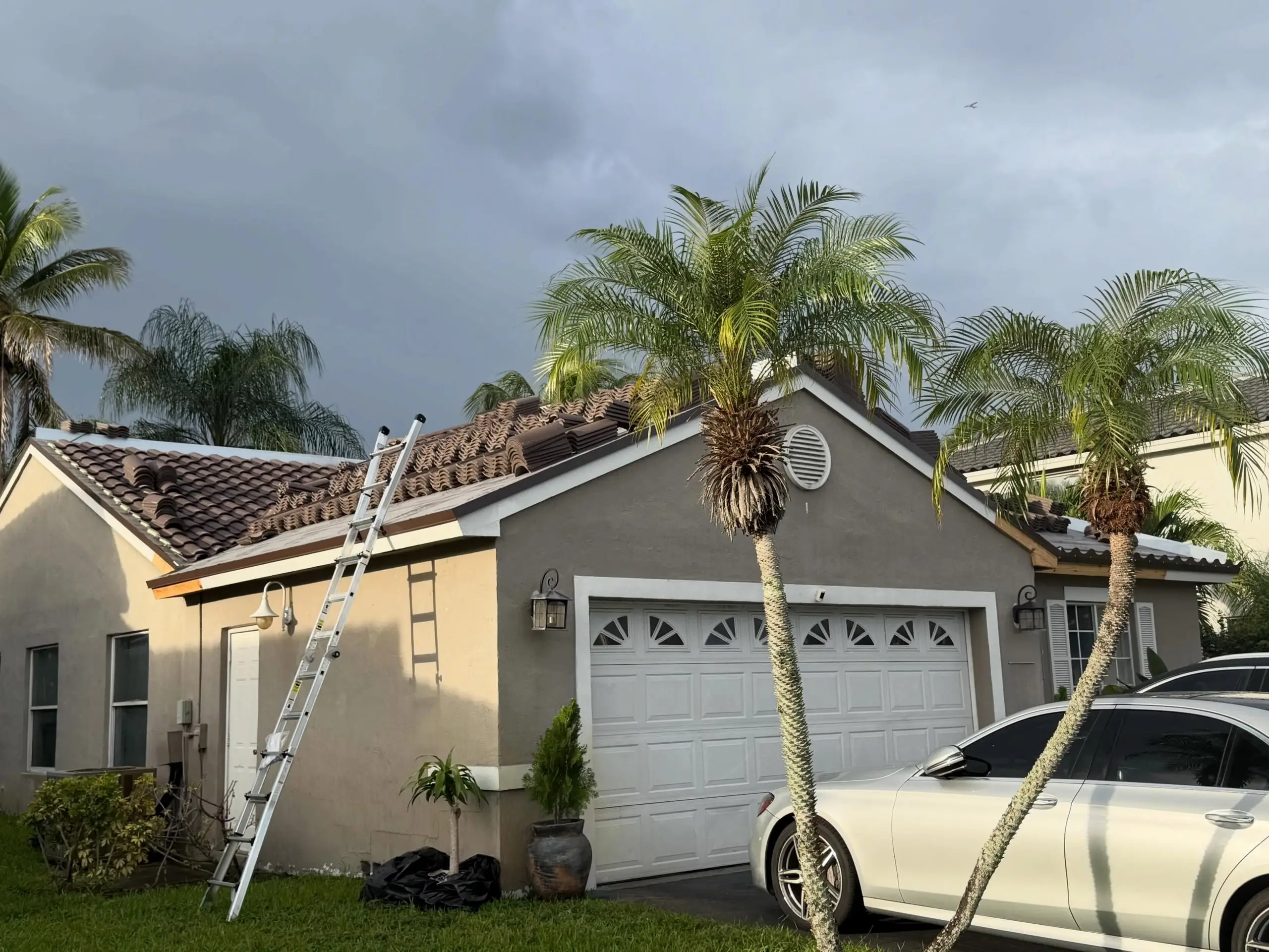 Tile roof installation in progress on a Chapel Trail home in Pembroke Pines, with a ladder at the eave and palms against a dark sky