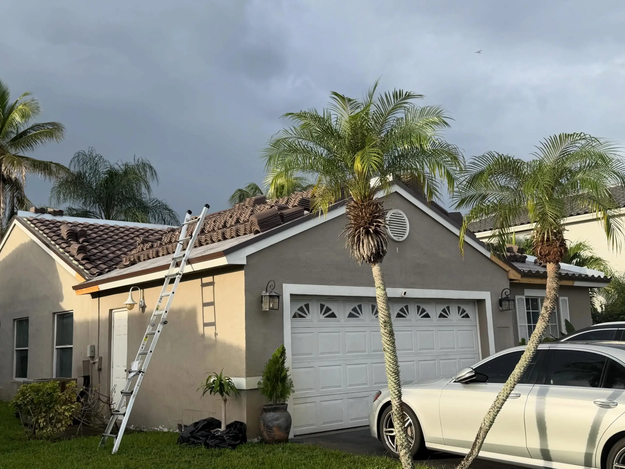 Tile roof installation in progress on a Chapel Trail home in Pembroke Pines, with a ladder at the eave and palms against a dark sky