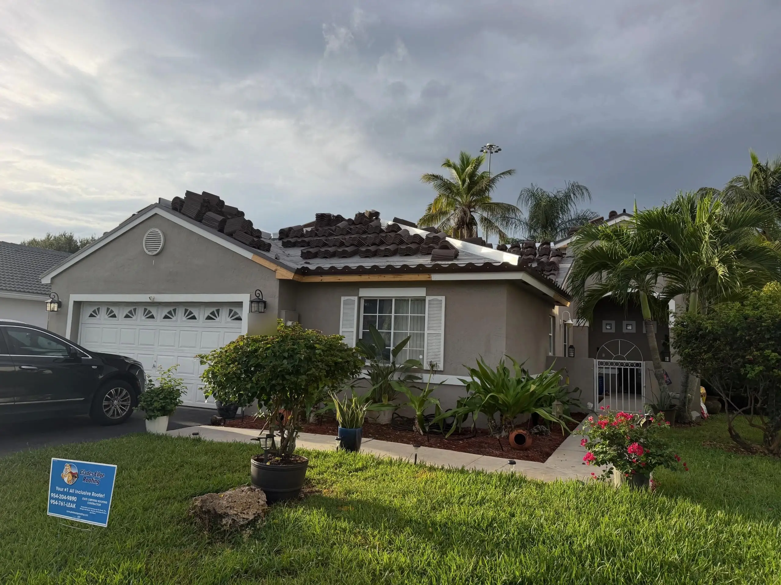 Gray stucco home in Chapel Trail, Pembroke Pines, with brown Eagle Capistrano roof tiles stacked on new underlayment under a stormy sky