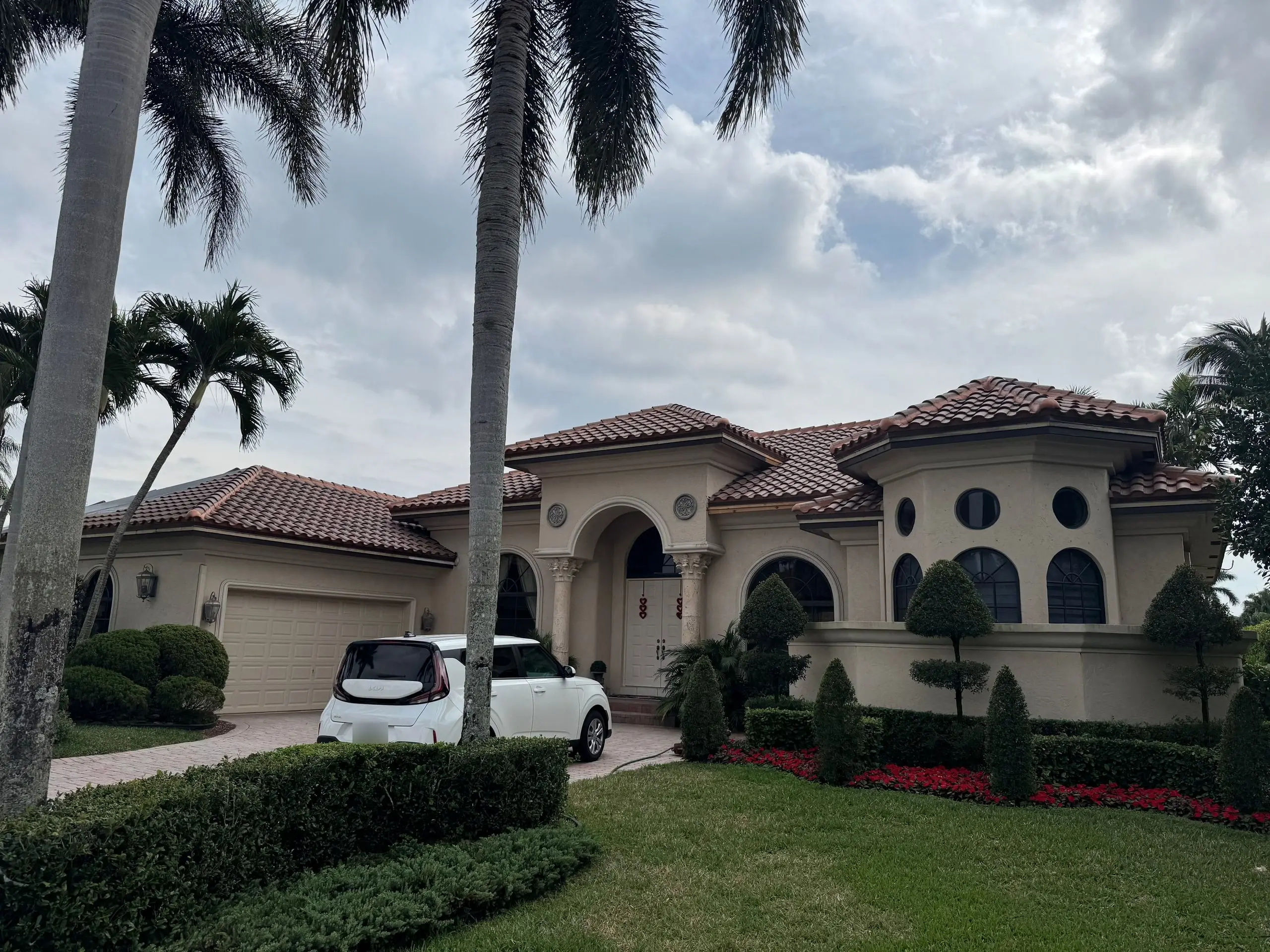Mediterranean-style stucco home with a finished terracotta barrel-tile roof, round and arched windows and a manicured yard with red flowers
