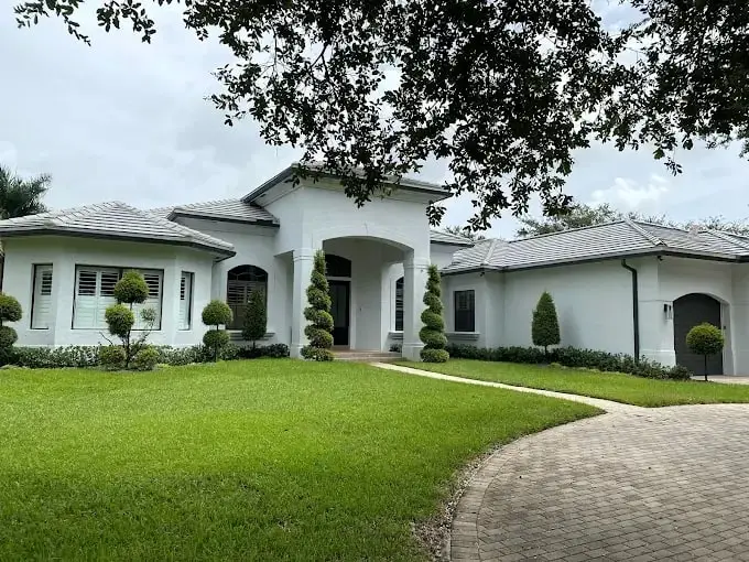 White single-story home with a finished gray flat-tile roof, a manicured lawn and a paver walkway