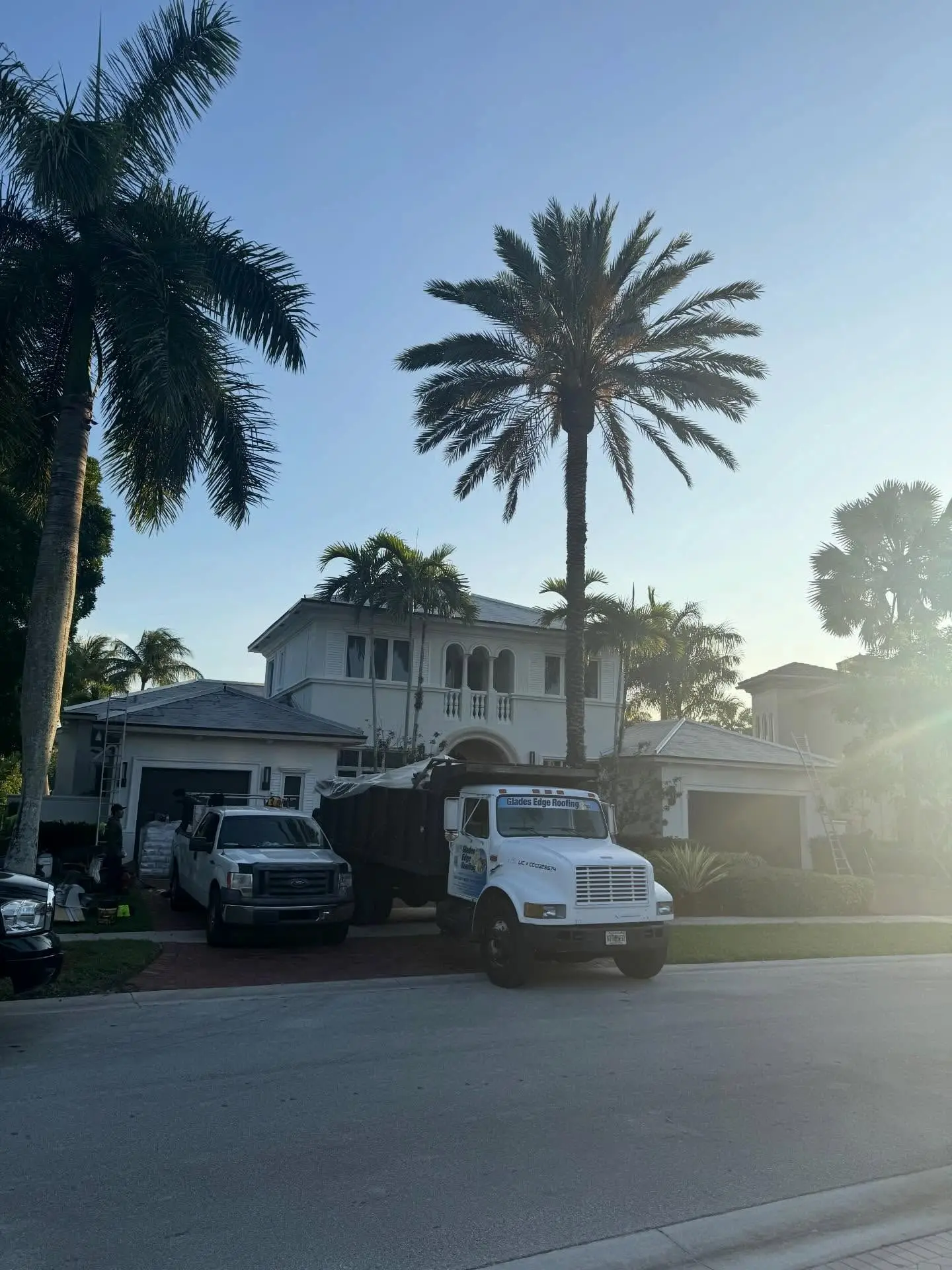 Glades Edge Roofing trucks parked in front of a two-story home in Hawks Landing, Plantation, at sunrise
