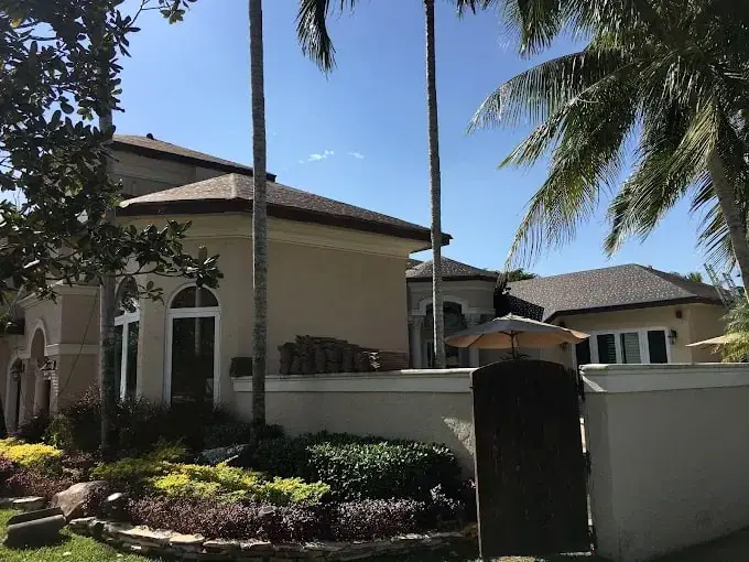 Mediterranean-style home with a gray tile roof behind a stucco wall and palms