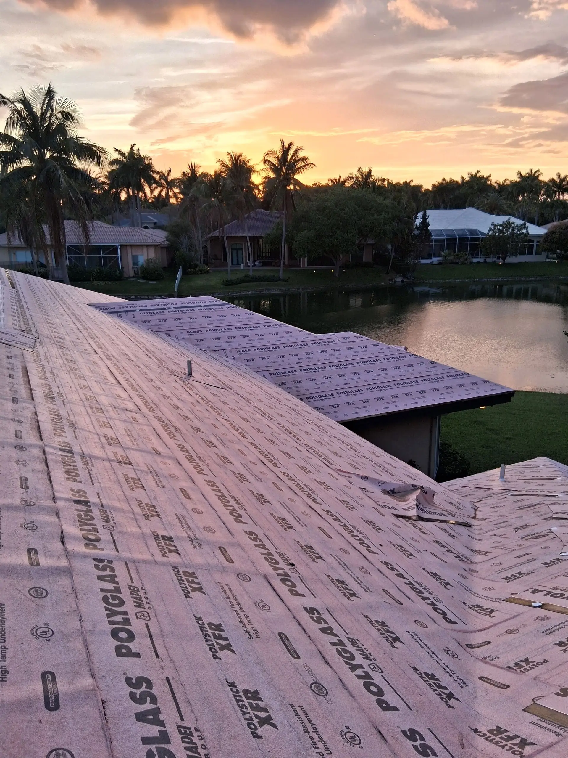 Pink Polyglass underlayment laid in two layers across a roof at sunset, with palm trees and a lake behind