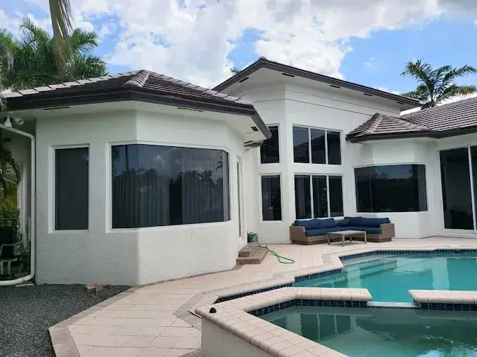 White modern home with a brown tile roof beside a pool and spa