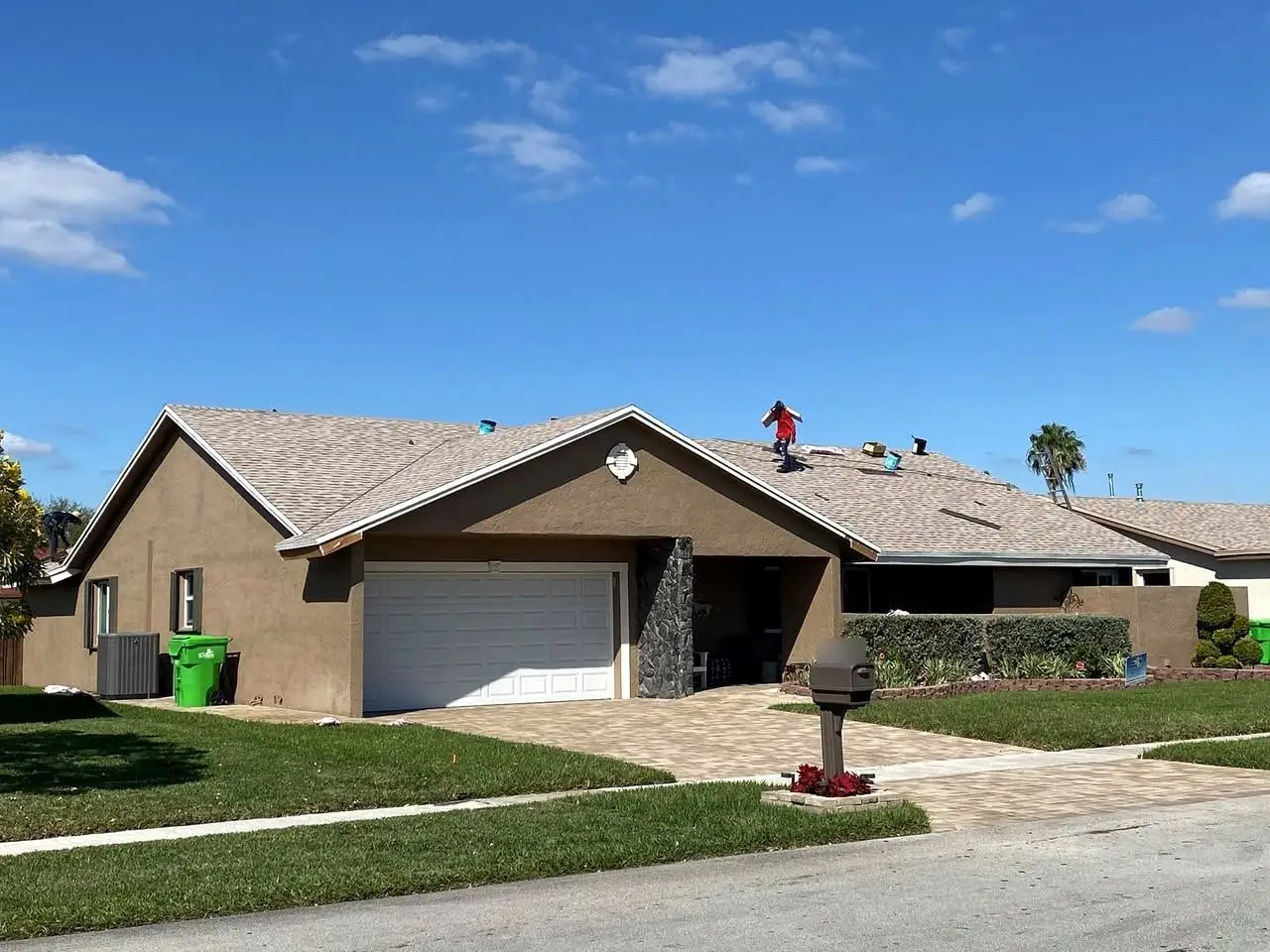 Roofer working across a light gray shingle roof on a brown single-story home