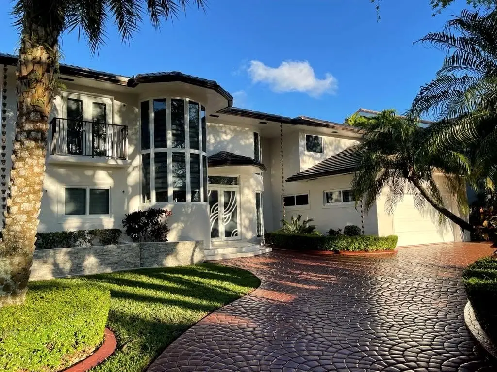 Large cream two-story Mediterranean home with a finished tile roof, palms and a curved paver driveway