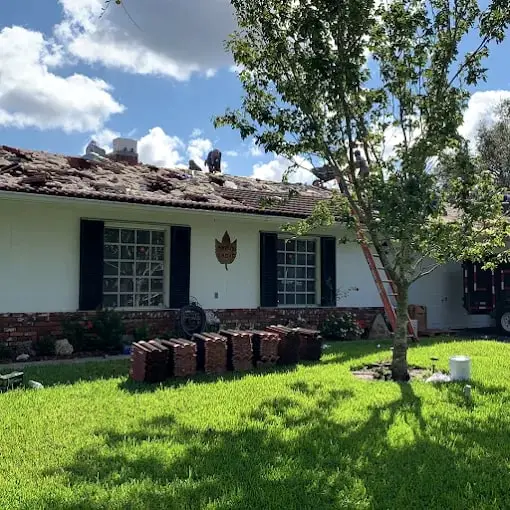 White home with its old tile roof removed and the tile stacked on the lawn